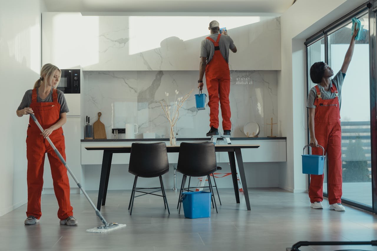 hero-gallery-03 Group of cleaners in red uniforms mopping and wiping glass in a modern dining room.