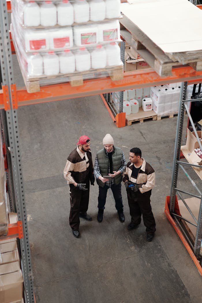 Three warehouse workers discuss logistics in an industrial storage facility.